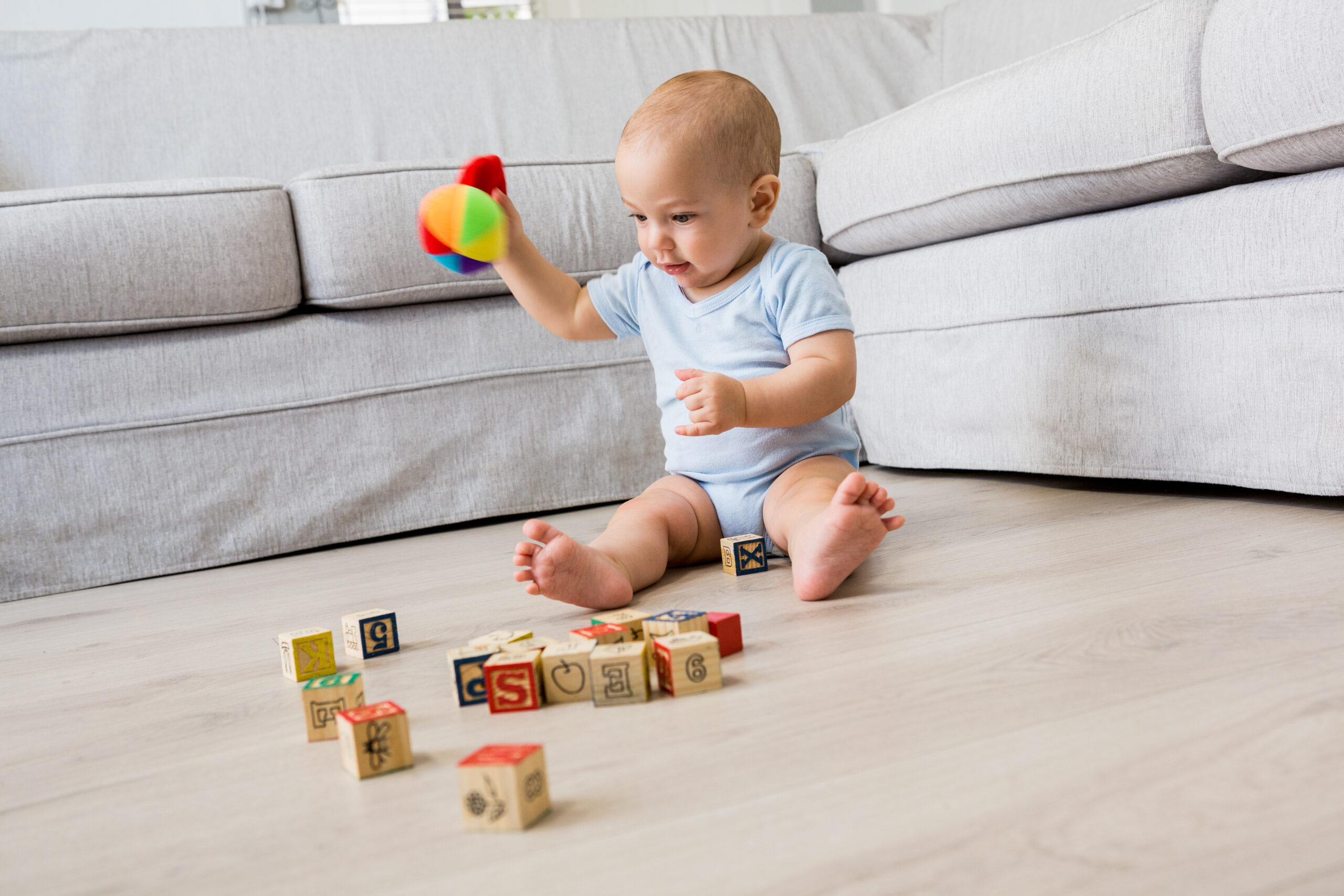Baby boy sitting on floor and playing with toys in living room at home